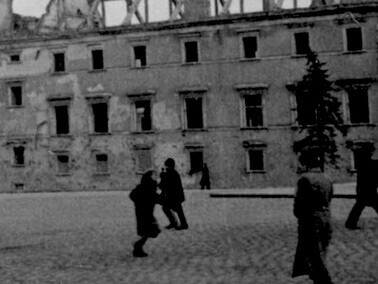 Passersby walking through Castle Square during World War II, with the ruins of the Royal Castle visible in the background, symbolizing the city’s wartime destruction, Warsaw, Poland