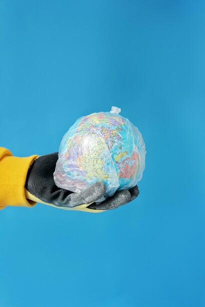 Hands grasp a world globe covered in plastic wrap, symbolizing pollution