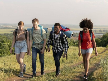 Four friends hike uphill with backpacks and smiles, showing that movement is more enjoyable with good company