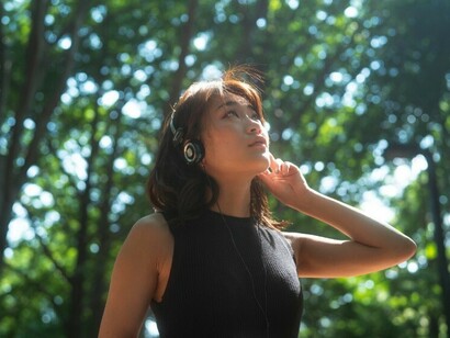 A thoughtful woman in silhouette, wearing headphones as she reflects quietly in a peaceful natural setting