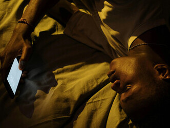 A young man lying in bed with his smartphone reflects the pandemic’s impact—endless screen time, social isolation, and rising depression among Gen Z