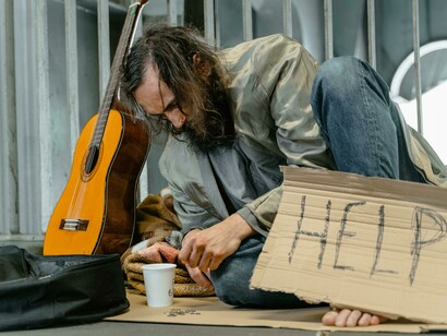 Bearded man sitting on the ground, asking for assistance