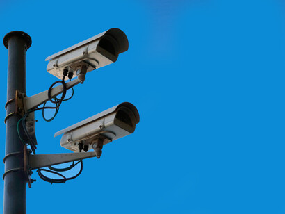 Two white CCTV cameras mounted on a black post under a clear blue sky