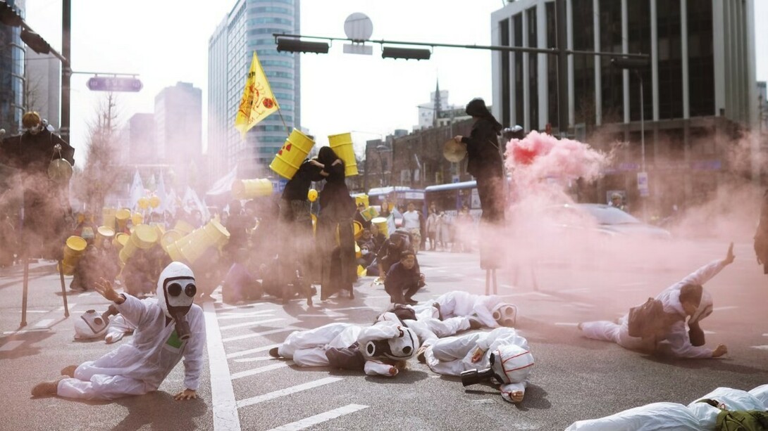 Protesters in scrub suits lie on the road surrounded by smoke during an anti-nuclear demonstration