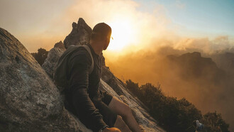 A man gazes at the sunset from a mountain peak, representing courage, growth, and stepping beyond the familiar Waikato, New Zealand