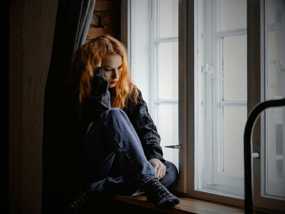 A solitary woman sitting next to the windows, surrounded by nothing but her thoughts