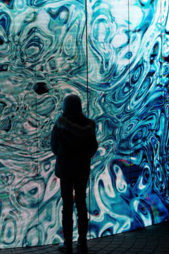 People gathered in front of a glowing blue wall at a nighttime digital art installation in Oslo, Norway