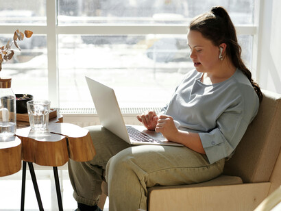 Seated comfortably on a couch, a girl with Down syndrome interacts with her laptop, demonstrating the accessibility of modern disability technology
