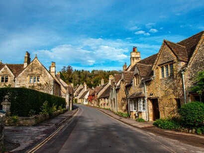 A street lined with charming old stone houses beneath a clear blue sky in Castle Combe, Chippenham, UK