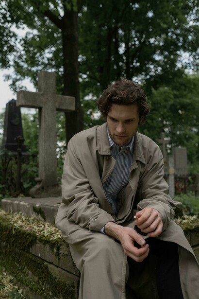 A man stands in a graveyard before a tombstone crowned with a cross, reflecting Christian tradition