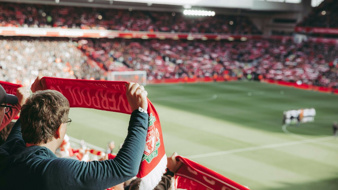 A fan holding a Liverpool scarf high in the stands
