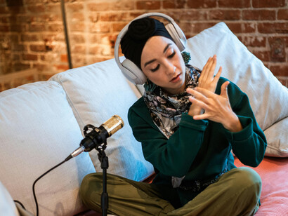 A content creator hosting a podcast, wearing white headphones and speaking into a microphone