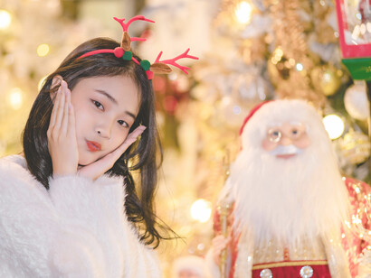 A woman with a reindeer headband poses next to a Santa figure during holiday shopping