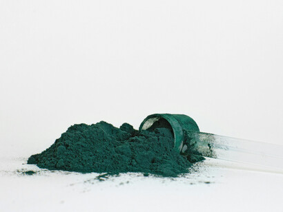 Bright green spirulina powder displayed on a white surface, sourced from nutrient-rich blue-green algae