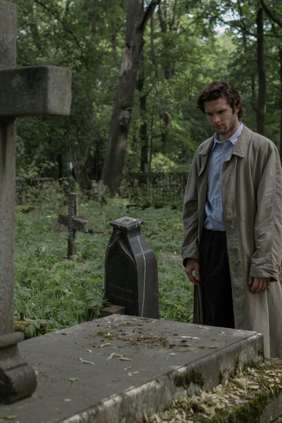 A man standing before a tombstone in a graveyard, marked with a cross, a symbol of Christianity