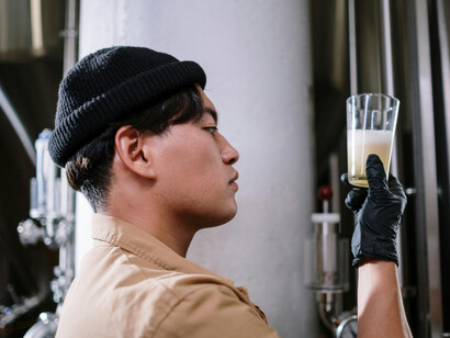 A man in a brown jacket and black knit cap savoring a glass of freshly brewed beer