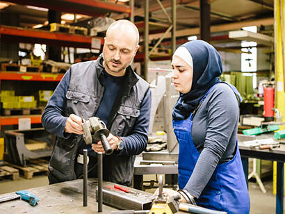In a German workshop, a young woman technician and a man collaborate, utilizing various work tools