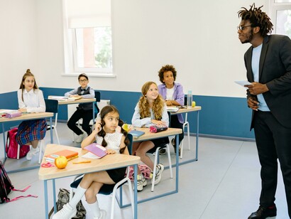 A male teacher works with students in a primary school classroom