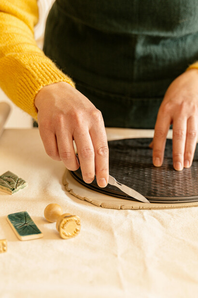 A person wearing an apron shapes a piece of clay while working on an art project