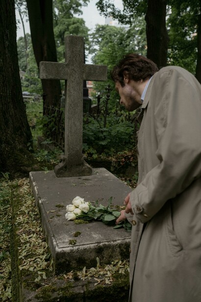 In a quiet cemetery, a man pauses before a cross-marked tombstone, symbolizing Christianity