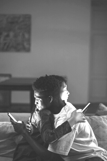 A pair lying side by side, each on their phone, illustrating modern disconnection and loneliness despite physical closeness