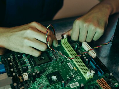 Dita che collegano cavi a una scheda madre verde del computer