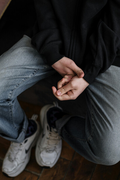 A solitary teenager dressed in dark clothing, with scars on his hands, sitting alone—symbolizing the emotional weight of anxiety, loneliness, and the pressures of growing up in the digital age