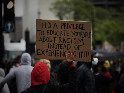 A man lifting a sign pointing out racism in the system, representing the continuous struggle for justice and the need for systemic reform to address discrimination in society