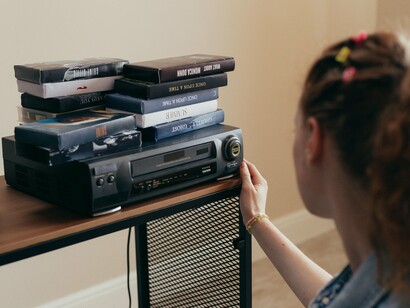 A girl adjusting a VCR beside a stack of tapes, representing the comfort found in predictable, well-known worlds