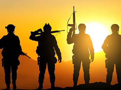 Armed militants moving through arid desert terrain at sunset