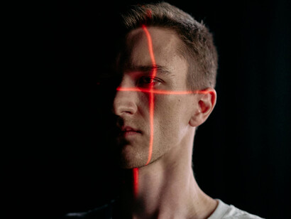 Portrait photo of a man with laser lines across his face, symbolizing government surveillance, biometric monitoring, and facial recognition systems
