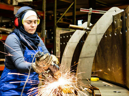 A young female technician and a male colleague work together in a workshop, handling tools, Germany