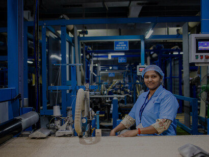 A smiling factory worker operates a textile machine, capturing the blend of craftsmanship and technology in today’s manufacturing industry