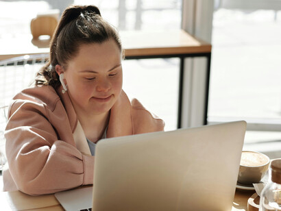 A girl with Down syndrome sits on a couch using a laptop, engaging with disability technology that supports her learning and independence