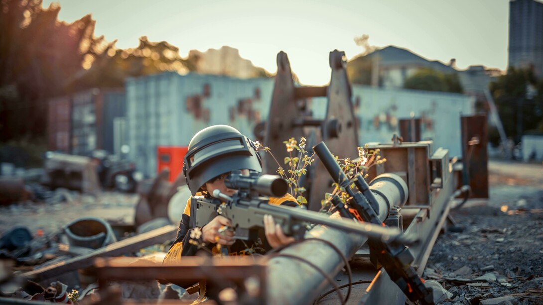 In a war zone, a man grips a rifle beside heavy machinery