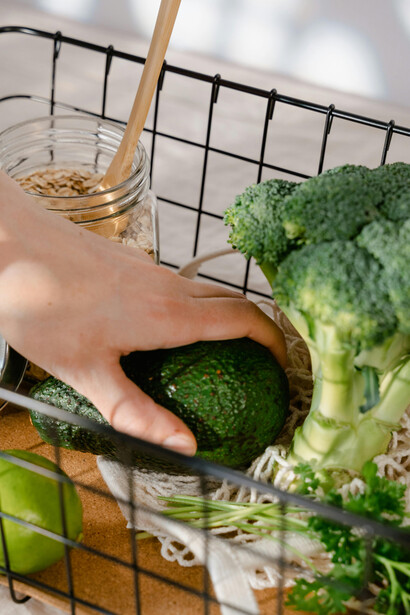 A person holds a fresh green avocado above a black steel basket, symbolizing antioxidant-rich foods, iron-packed plants, healthy superfoods, and natural supplements