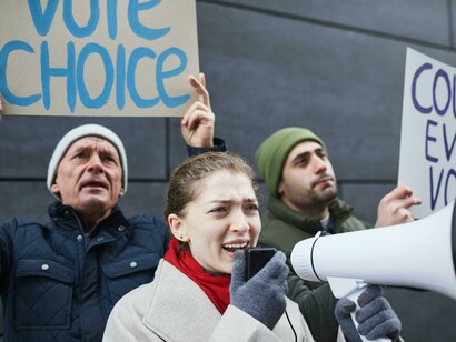 A woman raises a megaphone during a freedom of expression protest, representing the enduring importance of public discourse