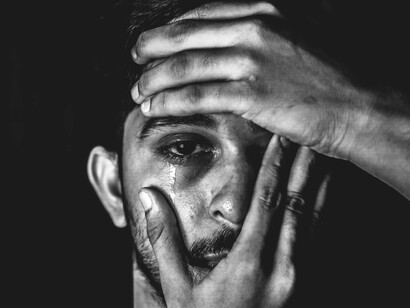 A man with tears streaming down while hands constrain his face, showing how grief often grasps us hard