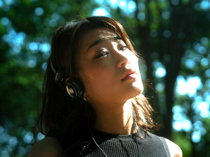 In a tranquil natural landscape, a silhouetted woman with headphones appears immersed in deep contemplation