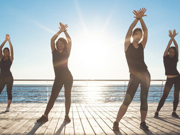 At sunrise, sportive women dancing Zumba by the sea demonstrate how physical activity enhances mental health