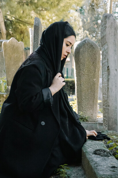 A woman in black clothing and hijab mourning in a graveyard, expressing Islamic grief and prayer