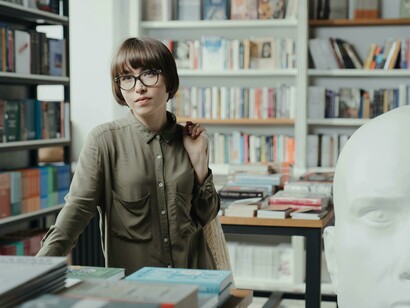 A woman browses through a stack of books in a cozy bookstore, surrounded by the quiet charm of a library—a haven for book lovers