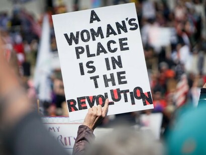 A woman holds a sign reading 'A Woman's Place Is in the Revolution' during the Hands Off protest against Donald Trump and Elon Musk outside the Utah State Capitol