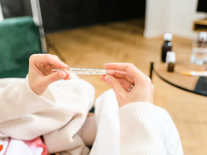 A person checking their temperature as medicines sit on the table, reflecting how people often turn to self-medication before seeking professional medical help for some illnesses