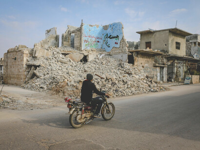 Idlib, Idlib Governorate, Syria. A biker rides through streets lined with destroyed houses in the aftermath of war