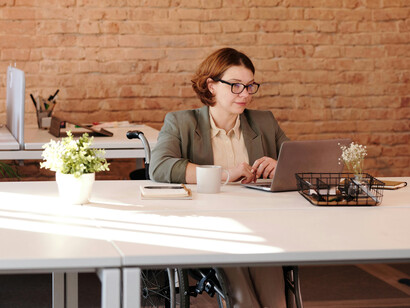 A woman with a disability smiling as she uses a laptop, seated comfortably in her wheelchair, showcasing independence and joy