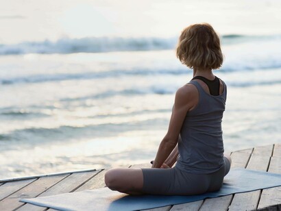 Una donna durante una meditazione al tramonto in riva al mare, seduta in posizione del loto su un pontile di legno