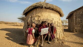 Maasai children using a laptop while sitting in a desert area of Tanzania, highlighting the contrast between poverty and access to technology