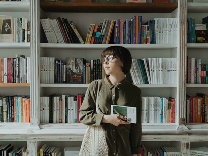 A woman leisurely browses a stack of books in a cozy bookstore that feels like a quiet library, perfect for any book lover