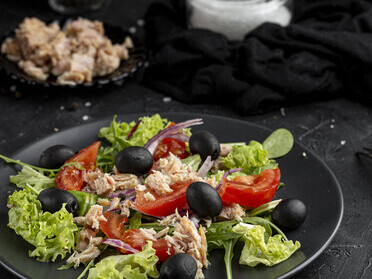 A wholesome Mediterranean meal featuring a homemade salad, salmon, and walnuts—served on a dark plate and rich in omega-3s